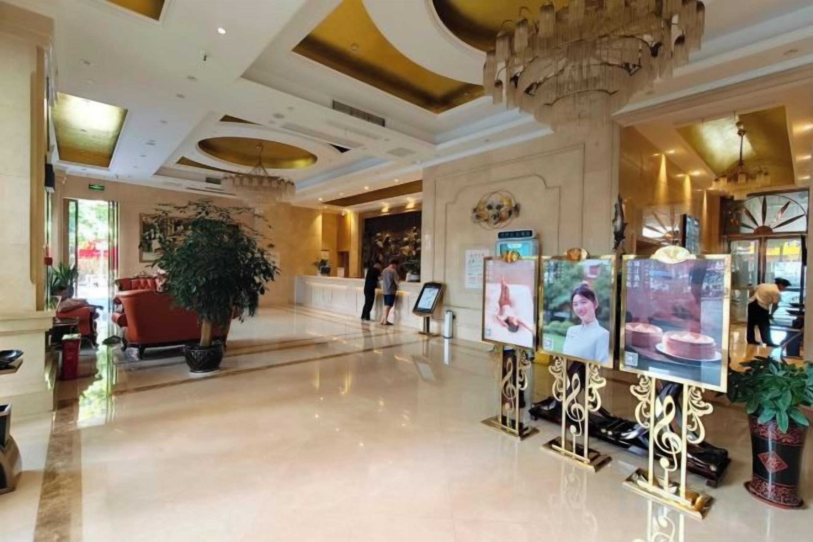 A hotel lobby with a reception desk, a large potted plant, and a chandelier.