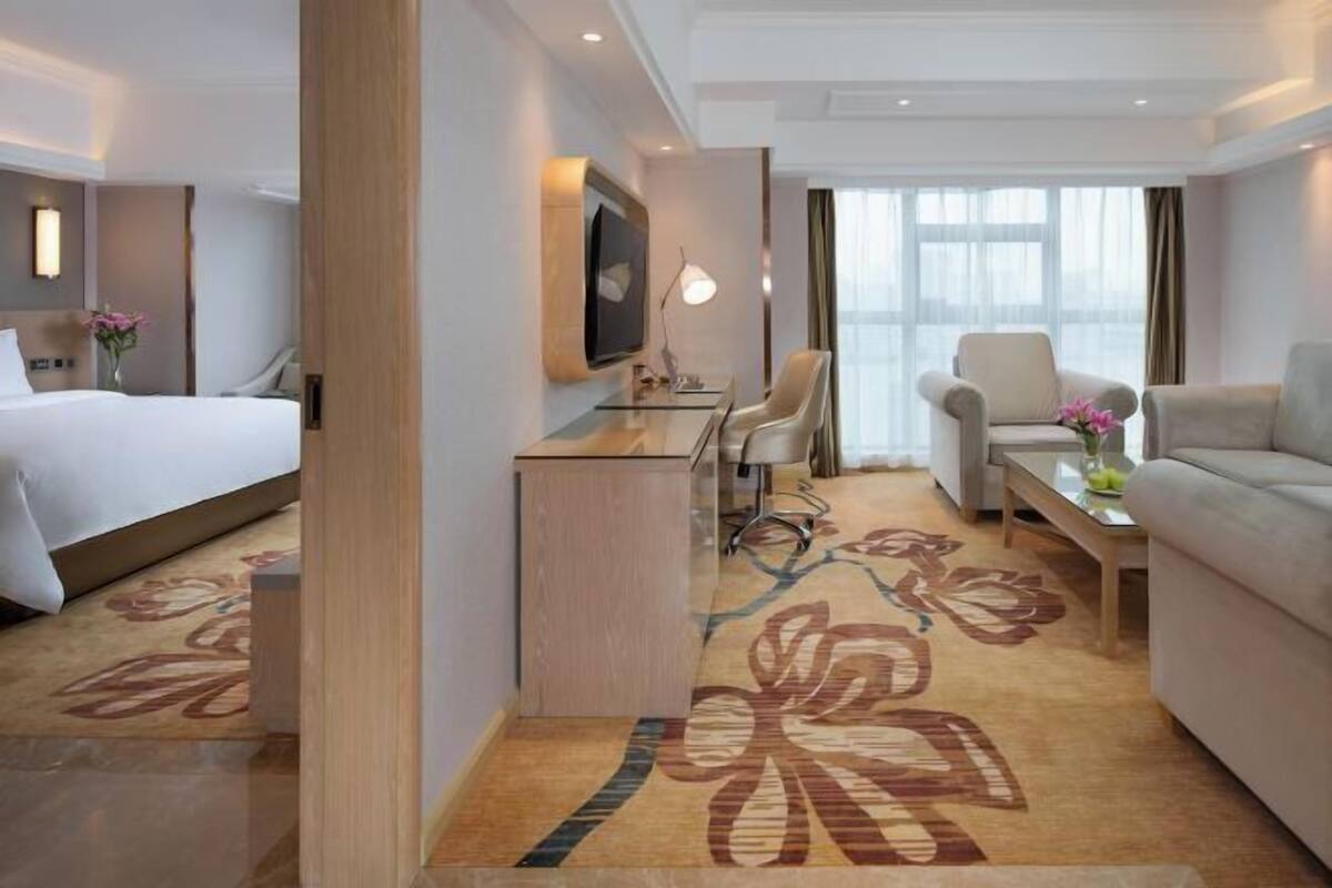 A hotel room with a bed, desk, two chairs, a sofa, and a large window with curtains.