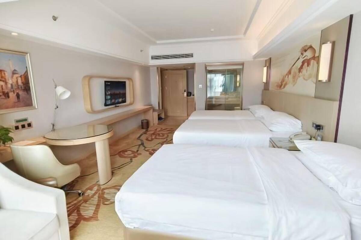 A hotel room with two beds, a desk, a chair, a TV, and a painting on the wall.