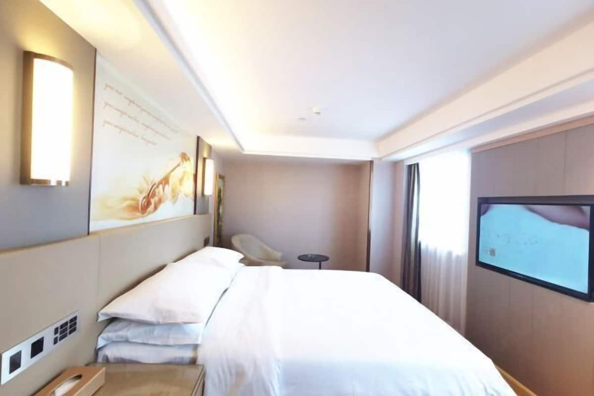 A hotel room with a bed, a TV, a desk, and a chair.