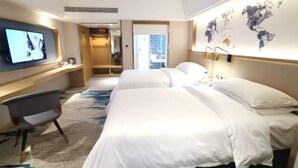 Habitación de hotel con dos camas, televisión, escritorio y un mapa mundial en la pared.