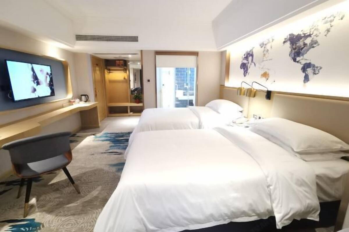 A hotel room with two beds, a TV, a desk, and a world map on the wall.