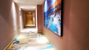 Un pasillo con alfombra estampada, un mural grande en la pared y una puerta al final.