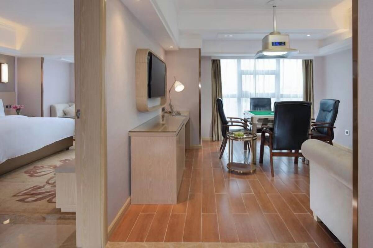 A hotel room with a bed, desk, chairs, and a TV.