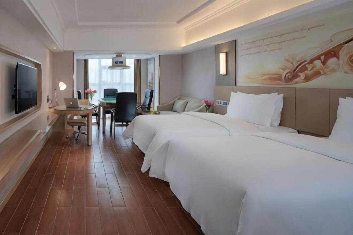 A hotel room with a large bed, a desk with a laptop, a chair, and a television.