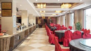 A hotel dining area with a check-in counter, multiple dining tables with red-covered chairs, and a checkered floor.