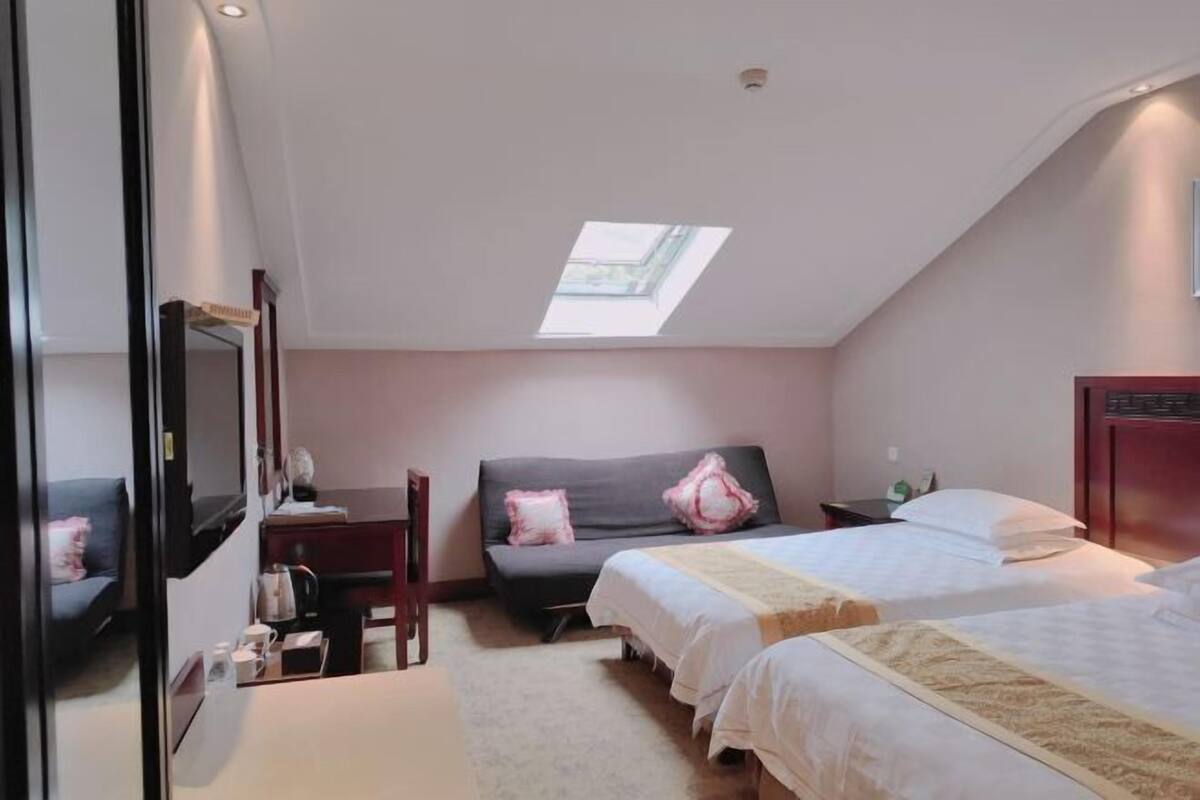A bedroom with a skylight, two beds, a desk, and a chair.