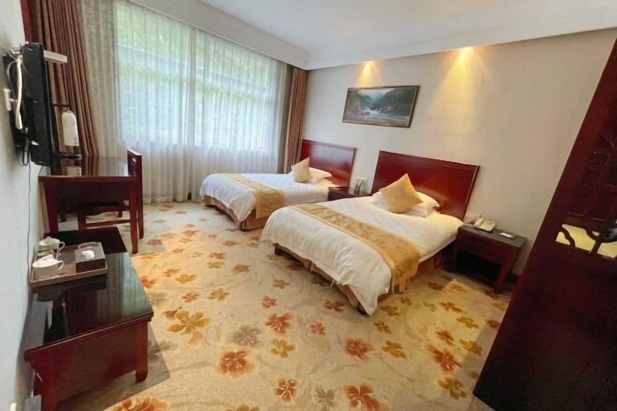 Une chambre d’hôtel avec deux lits, un bureau, une chaise, une petite table et un tableau au mur.