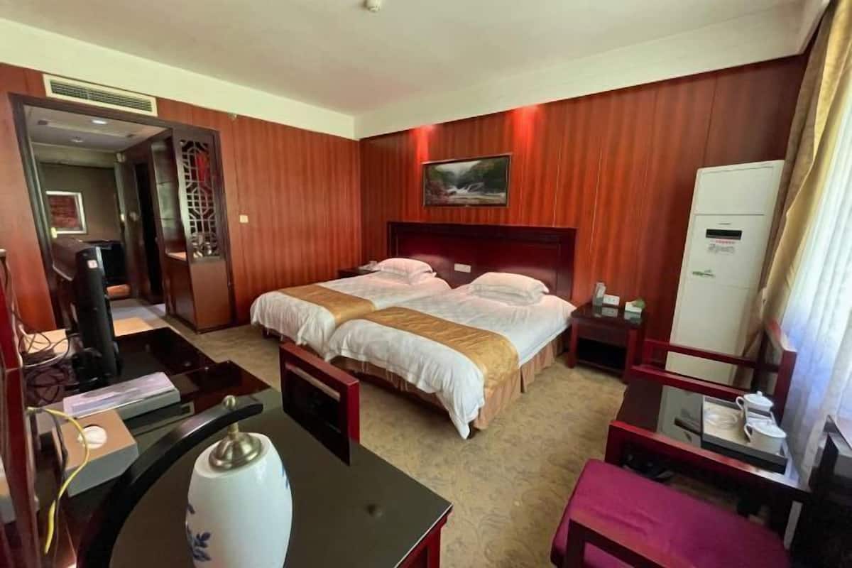 A hotel room with two beds, a desk, a chair, a TV, and a refrigerator.