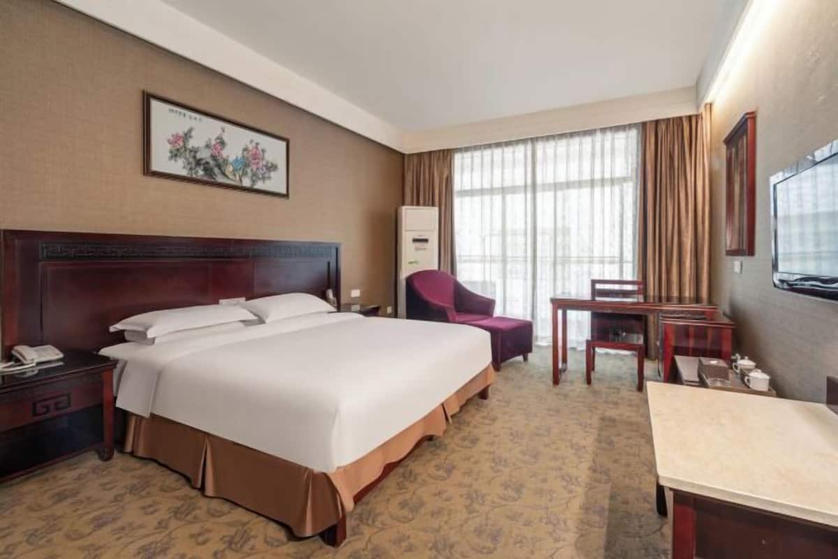 A hotel room with a large bed, a desk, a chair, a TV, and a painting on the wall.