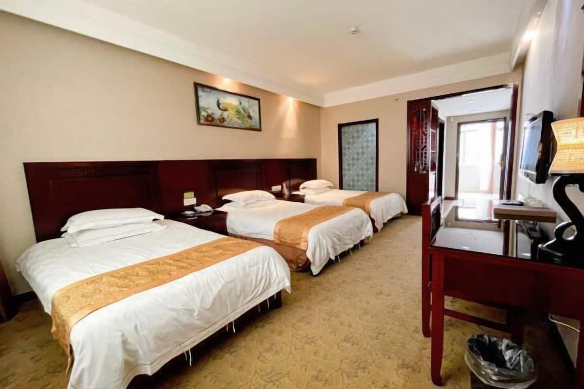 A hotel room with three beds, a desk, and a trash bin.