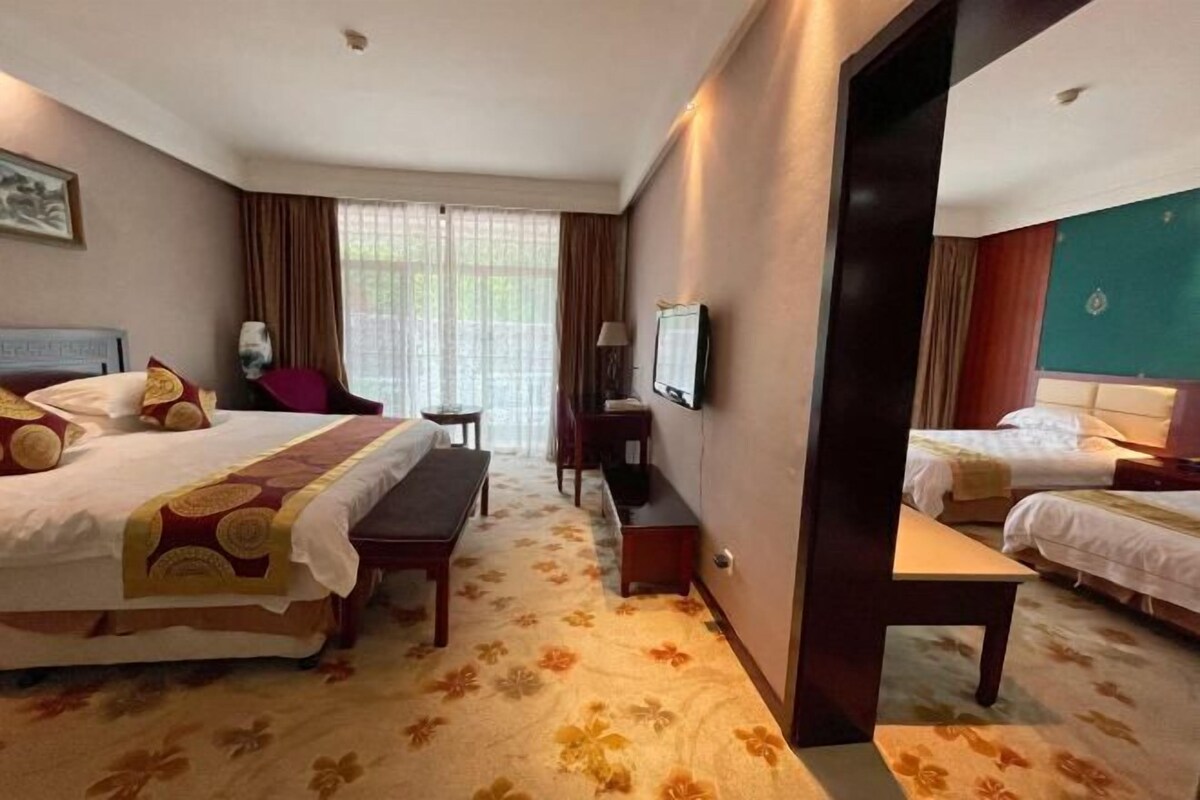 A hotel room with two beds, a desk, a chair, a TV, and a window with curtains.