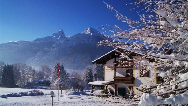 A mountain lodge with a wooden exterior, a covered porch, and a view of snow-covered mountains.