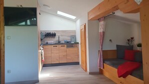 A compact living space with a kitchenette, a wooden bench with cushions, and a view of the kitchen.