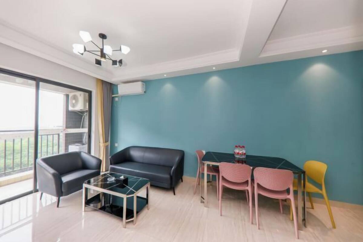 A modern living room with a black leather sofa, a glass coffee table, and a dining table with colorful chairs.