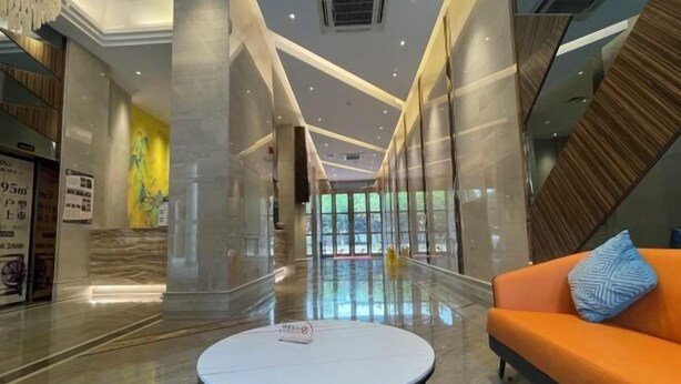 A modern hotel lobby with a marble floor, a round white table, and an orange sofa with a patterned pillow. - Foshan Leshui Mansion (Leliu Port West Road Branch) (Foshan)