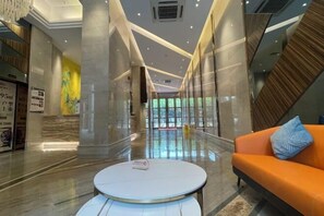 A modern hotel lobby with a marble floor, a round white table, and an orange sofa with a patterned pillow. - Foshan Leshui Mansion (Leliu Port West Road Branch) (Foshan)