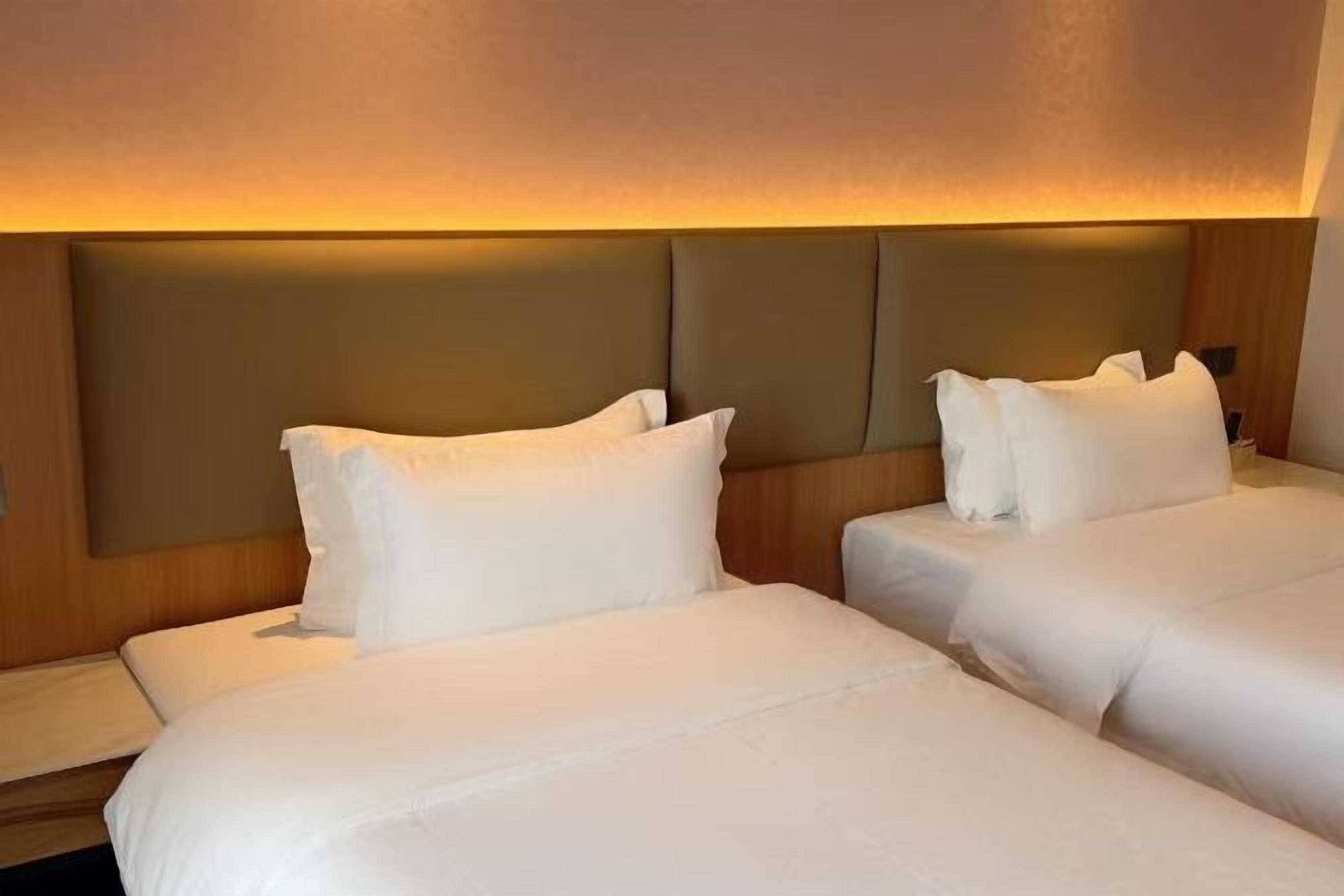 A hotel room with two beds, a wooden headboard, and a warm ambient light.