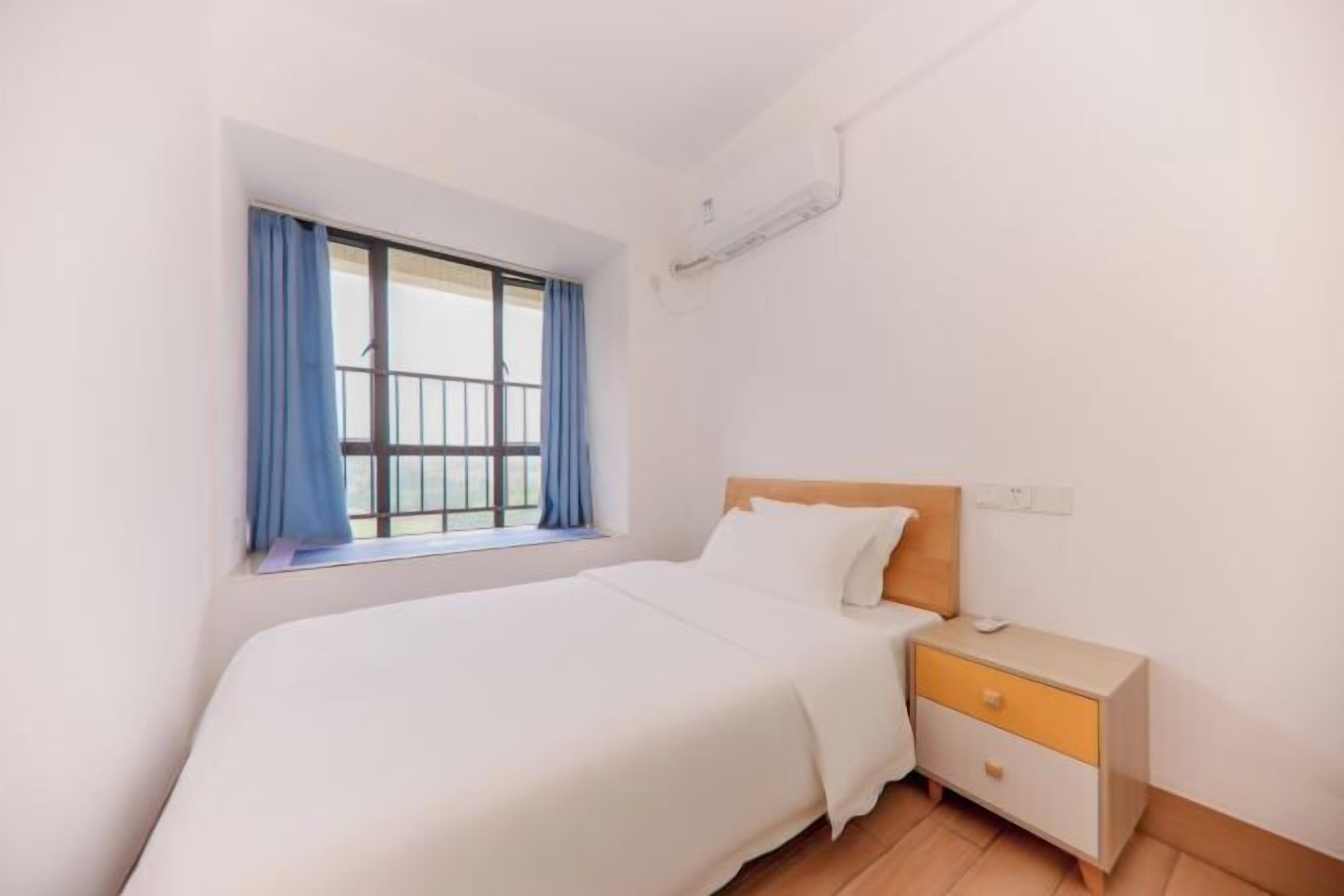 Ein Schlafzimmer mit Bett, Nachttisch, Fenster mit Vorhängen und einer Klimaanlage.