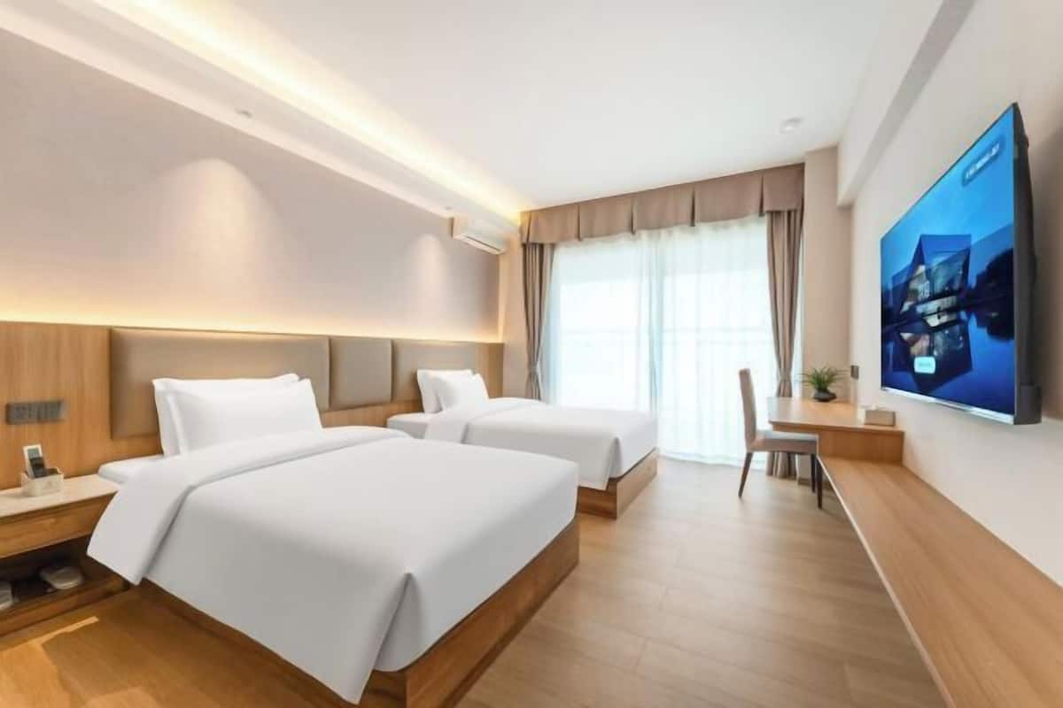A hotel room with two beds, a desk, a chair, a flat-screen TV, and a large window with curtains.