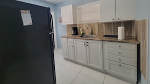 A kitchen with white cabinets, a black refrigerator, a sink, and a countertop with a coffee maker. - Cute Paradise 2 (Tampa)