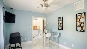 A room with a ceiling fan, a TV mounted on the wall, a kitchenette, and a dining area with a small table and chairs. - Cute Paradise 2 (Tampa)