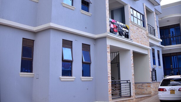 A multi-story residential building with a balcony on the second floor, a garage door, and a car parked in front. - Stunning 2-Bed Apartment in Namugongo Town Kampala (Namugongo Town)
