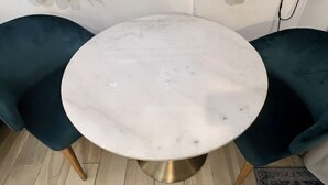 Ein runder Tisch mit weißer Marmorplatte, umgeben von zwei Sitzstühlen in Türkis mit Holzbeinen.