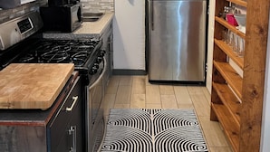 Eine kleine Küche mit einem Edelstahl-Kühlschrank, einem Gasherd und Holzregalen.