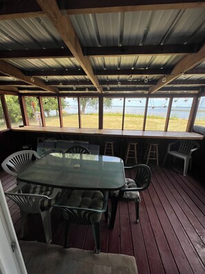 An outdoor covered patio with a glass table and chairs, wooden beams, and a view of a body of water. - Home with panoramic lake views of Lake Poygan  (Winneconne)