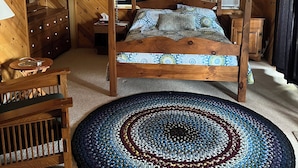 Un lit à baldaquin en bois, surmonté d’une couvre-lit à motifs, un tapis rond et un ventilateur de plafond dans une pièce aux murs en bois et dotée d’une fenêtre avec des rideaux.