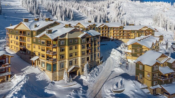 Un hotel de varios pisos con fachada de piedra, múltiples balcones y un paisaje cubierto de nieve.