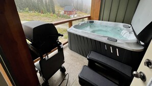 Un jacuzzi en un balcón con vistas a un bosque y un edificio lejano.