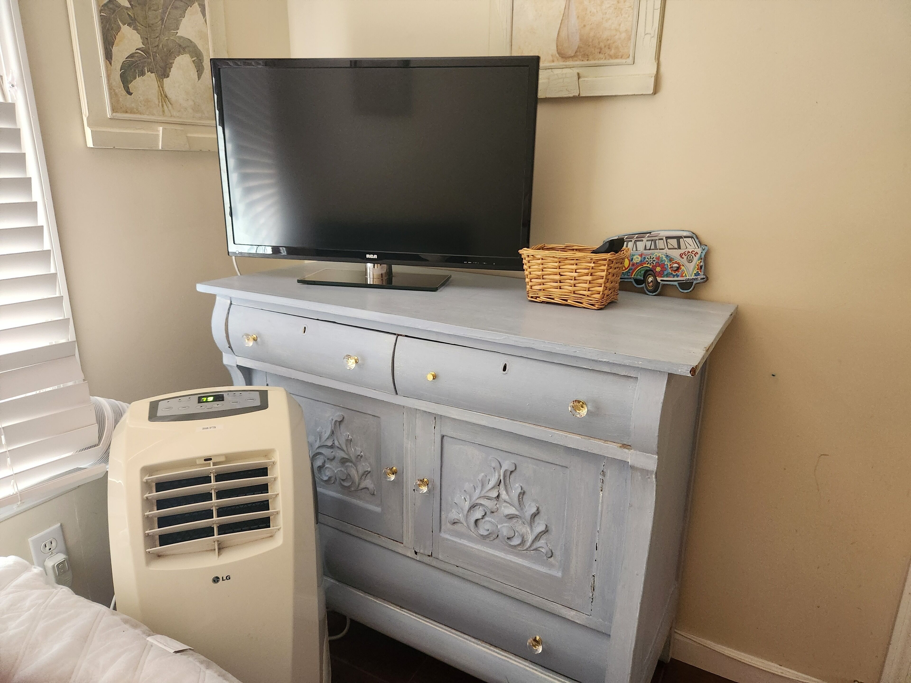 A room with a TV on a dresser, a wicker basket, and a vintage car model.