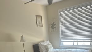 Ein Schlafzimmer mit zwei Betten, einem Nachttisch, einer Lampe, einem Fenster mit Jalousien und einem gemusterten Teppich.