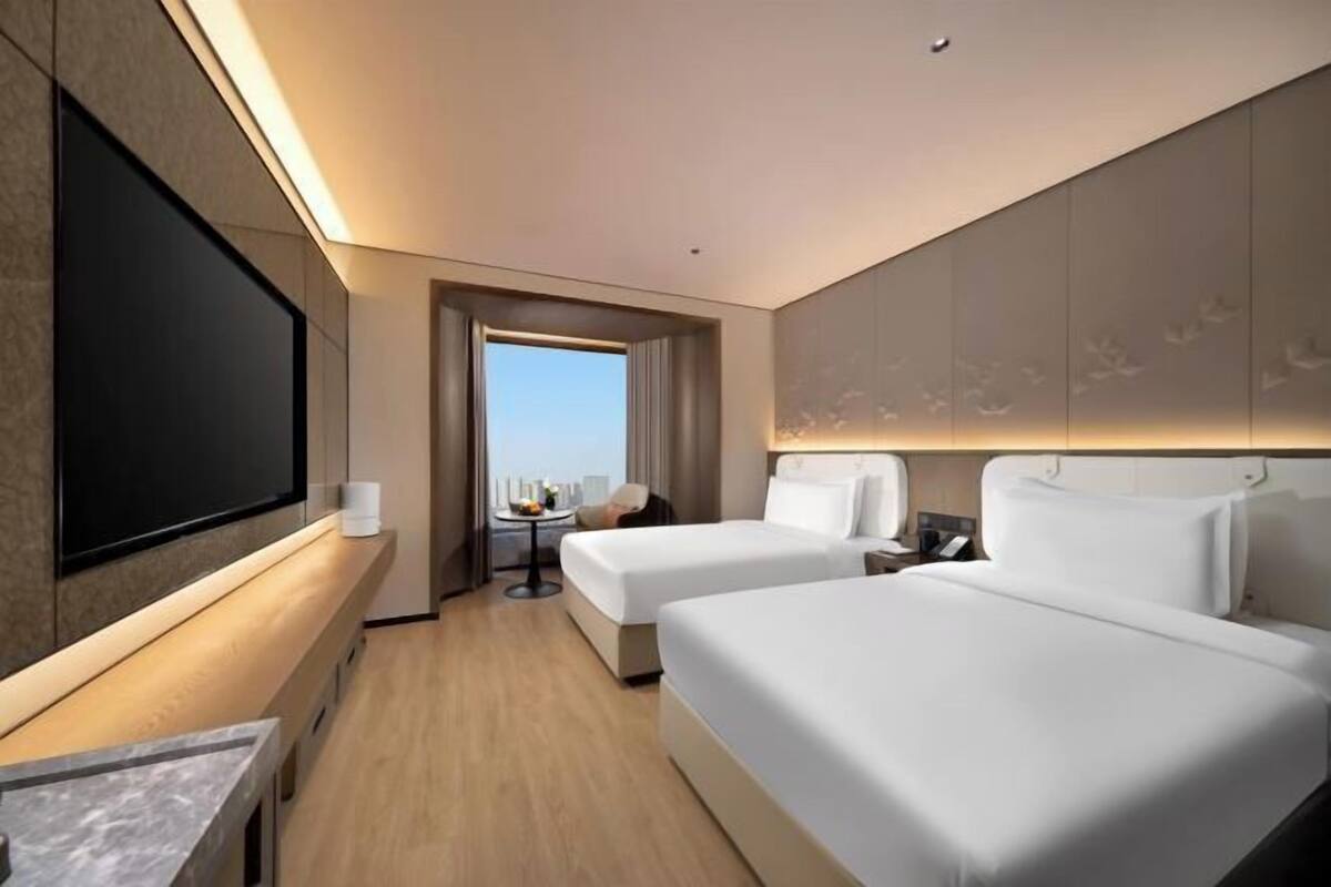Ein Hotelzimmer mit zwei Betten, einem Fernseher, einem Schreibtisch und Blick auf die Stadt.