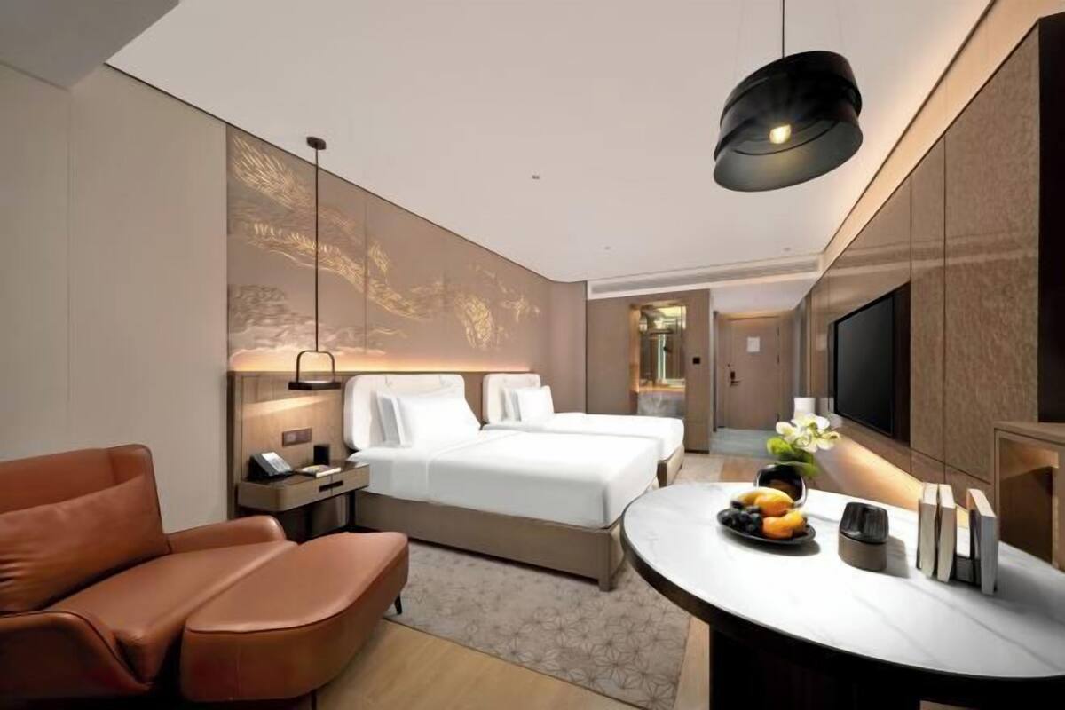 Ein modernes Hotelzimmer mit Bett, einer Couch, einem Schreibtisch mit Obstschale und einem Fernseher.