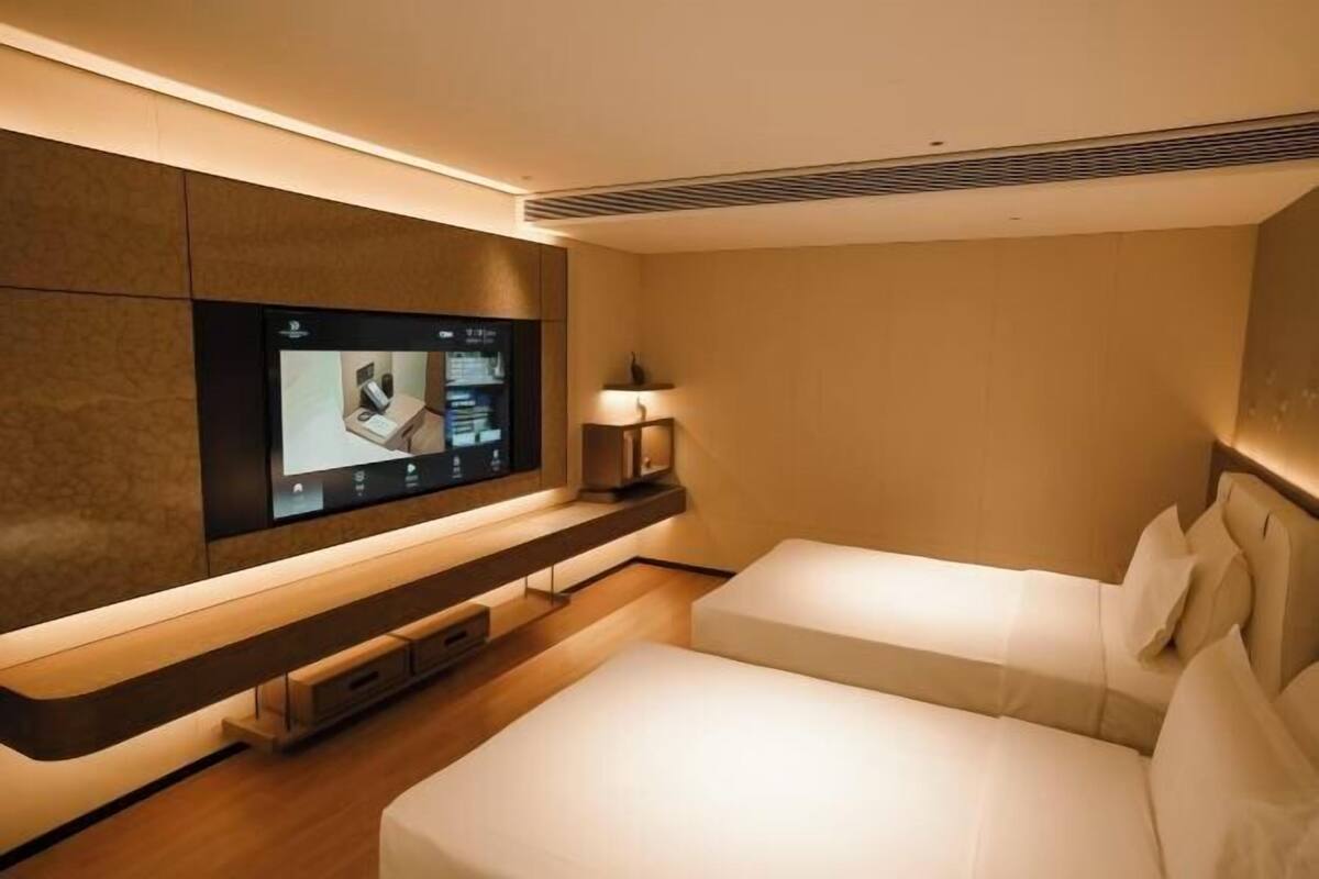 Ein modernes Hotelzimmer mit einem an der Wand befestigten Flachbildfernseher, einem Nachttisch mit Lampe und zwei Betten.