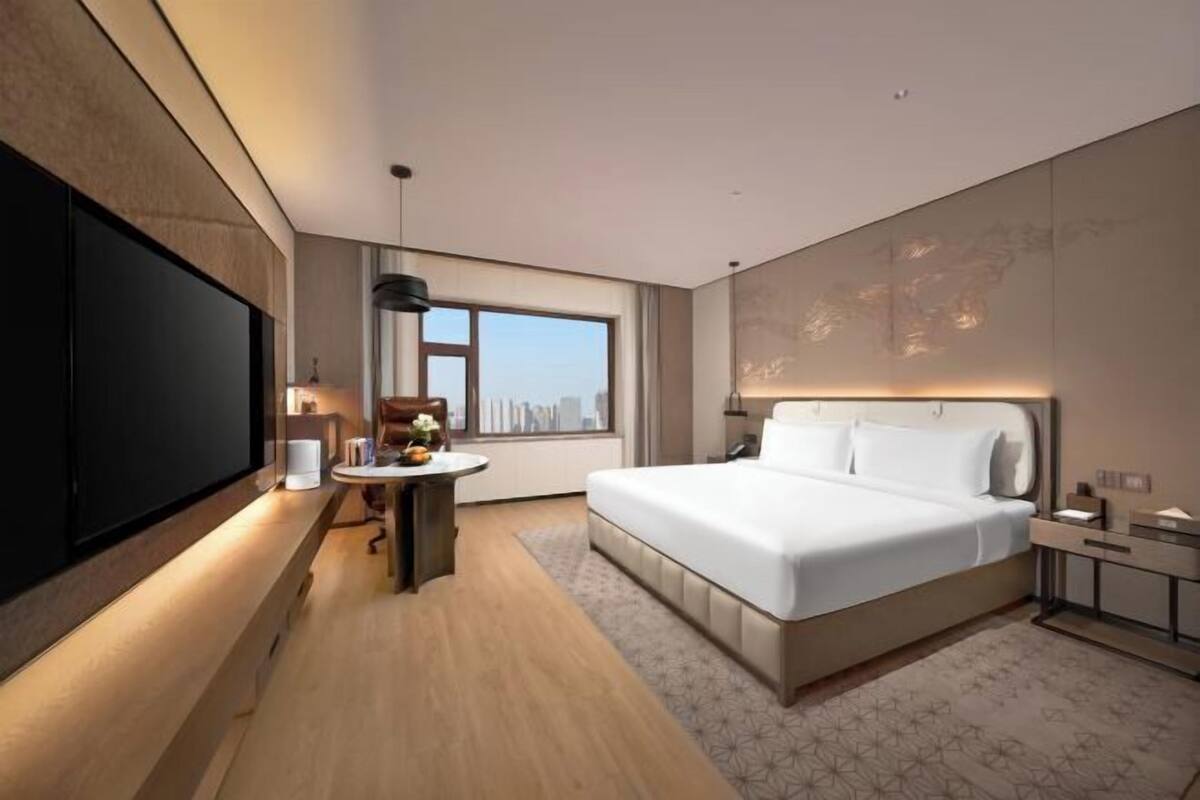 Ein modernes Hotelzimmer mit einem großen Bett, einem Flachbildfernseher, einem Schreibtisch mit Lampe und Blick auf die Stadt.