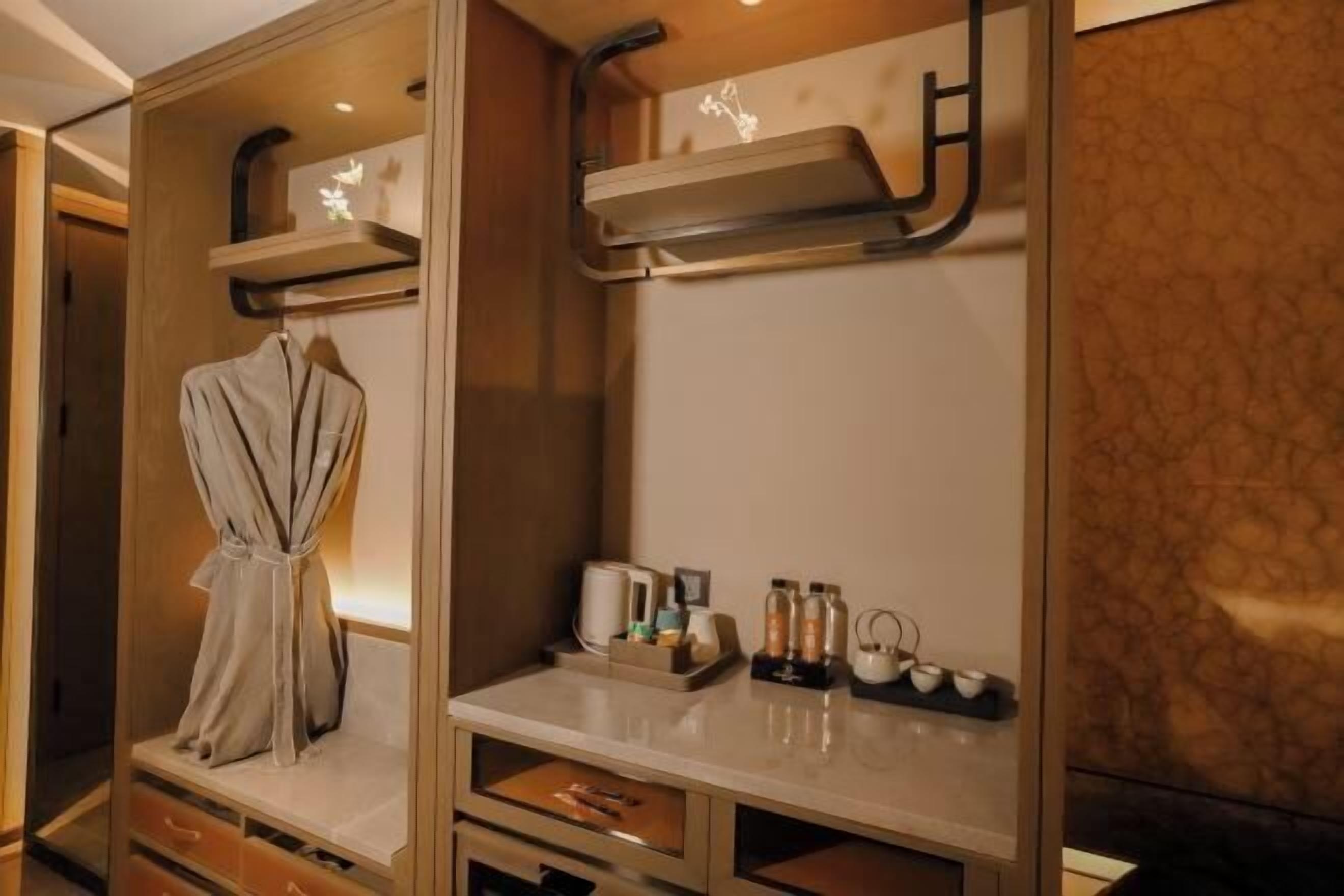 Hotelkamer met een badjas aan een rek, een kaptafel met toiletartikelen en een plank met een handdoek.