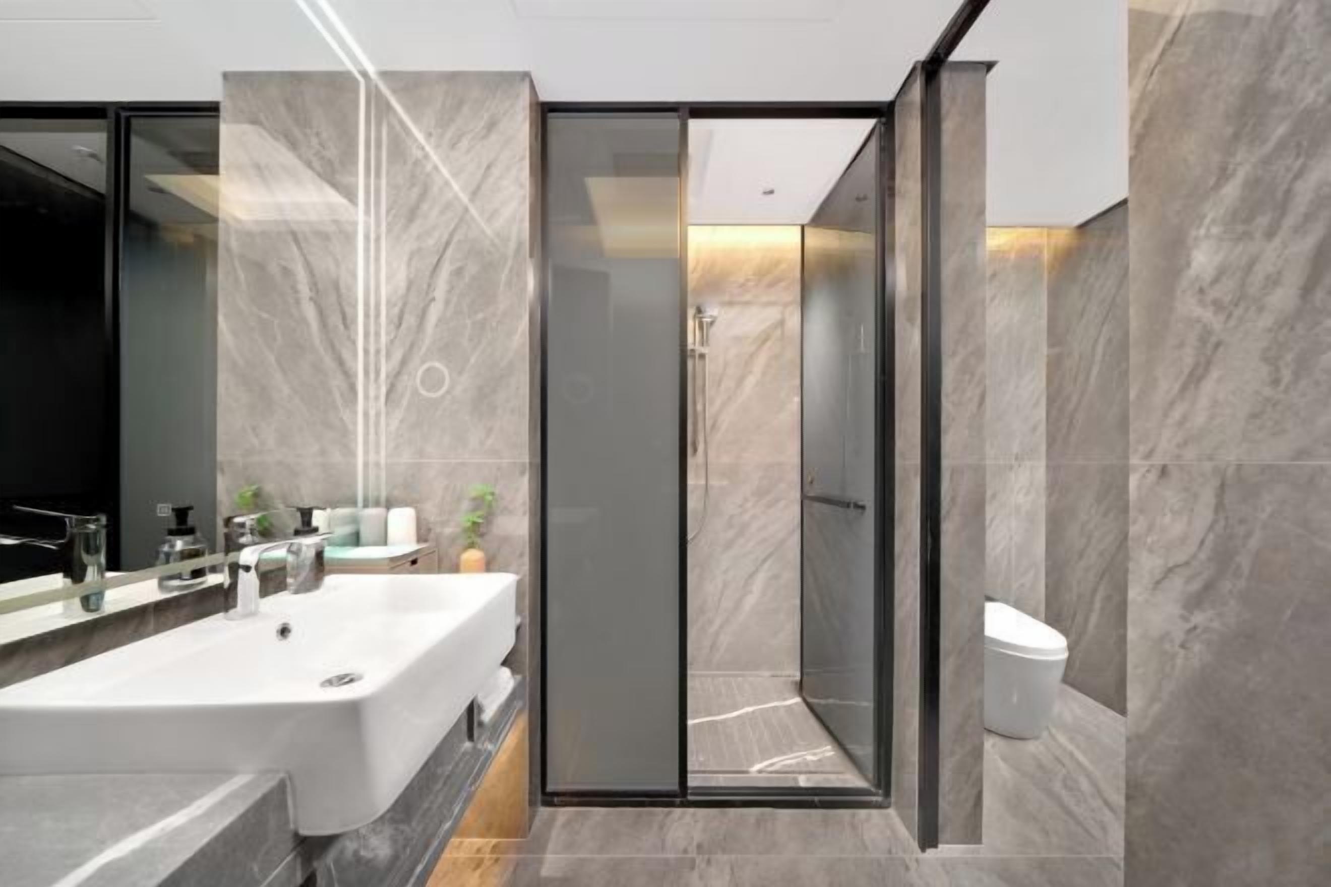 A modern bathroom with a large sink, a glass shower enclosure, and marble walls.