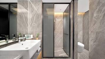 A modern bathroom with a large sink, a glass shower enclosure, and marble walls.