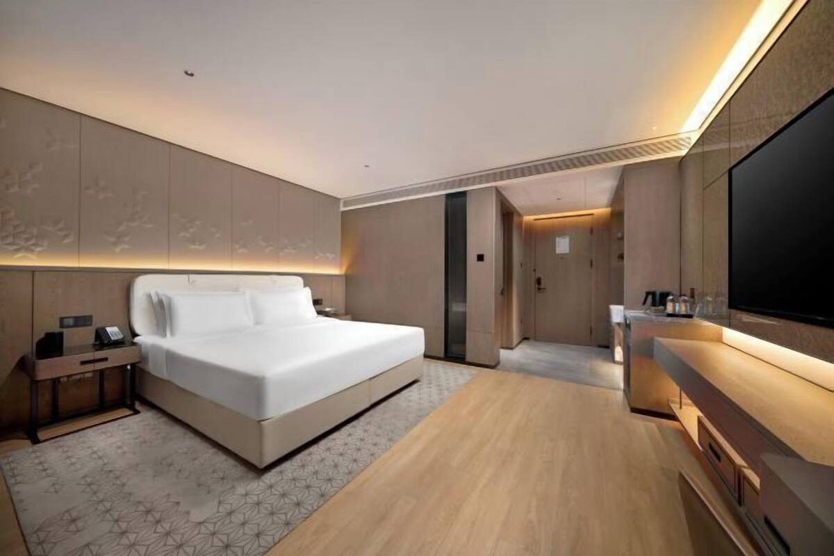 Ein modernes Hotelzimmer mit einem großen Bett, einem Flachbildfernseher, einem Holztisch und einem großen Spiegel.