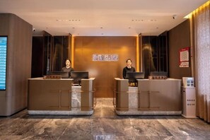 A hotel reception area with two receptionists at desks, a digital display, and a sign above the desks. - Shunda Shuihui Hotel (Kedong)