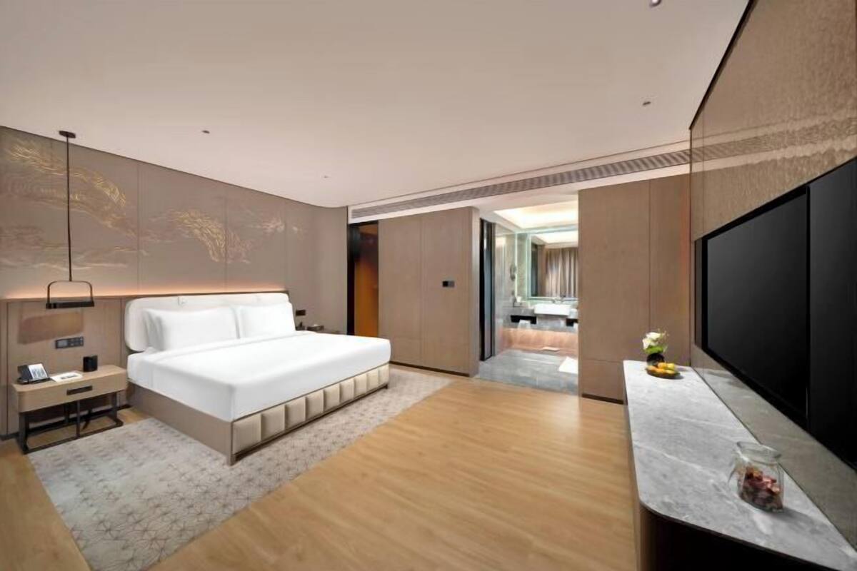 Ein modernes Hotelzimmer mit einem großen Bett, einem Flachbildfernseher, einem Schreibtisch und einem durch eine offene Tür einsehbaren Badezimmer.