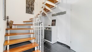 Un escalier avec des marches en bois et des rampes blanches, un radiateur fixé au mur et un petit meuble avec une étagère.
