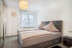 Une chambre à coucher comprenant un lit, une table de chevet, un miroir, une fenêtre avec des rideaux et un élément décoratif mural.