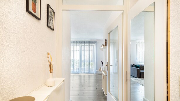 A hallway with a white wall, a white door, and a white shelf with a bowl and a vase. - Apartment 'Tulips' with Shared Garden, Balcony and Wi-Fi (Meckenbeuren)