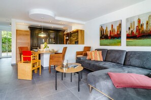 A modern living room with a sofa, a dining area with chairs, and a kitchen area with cabinets.
