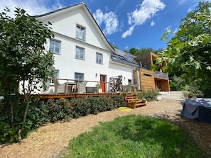 A two-story building with a white exterior, a balcony with wicker furniture, and a red door.
